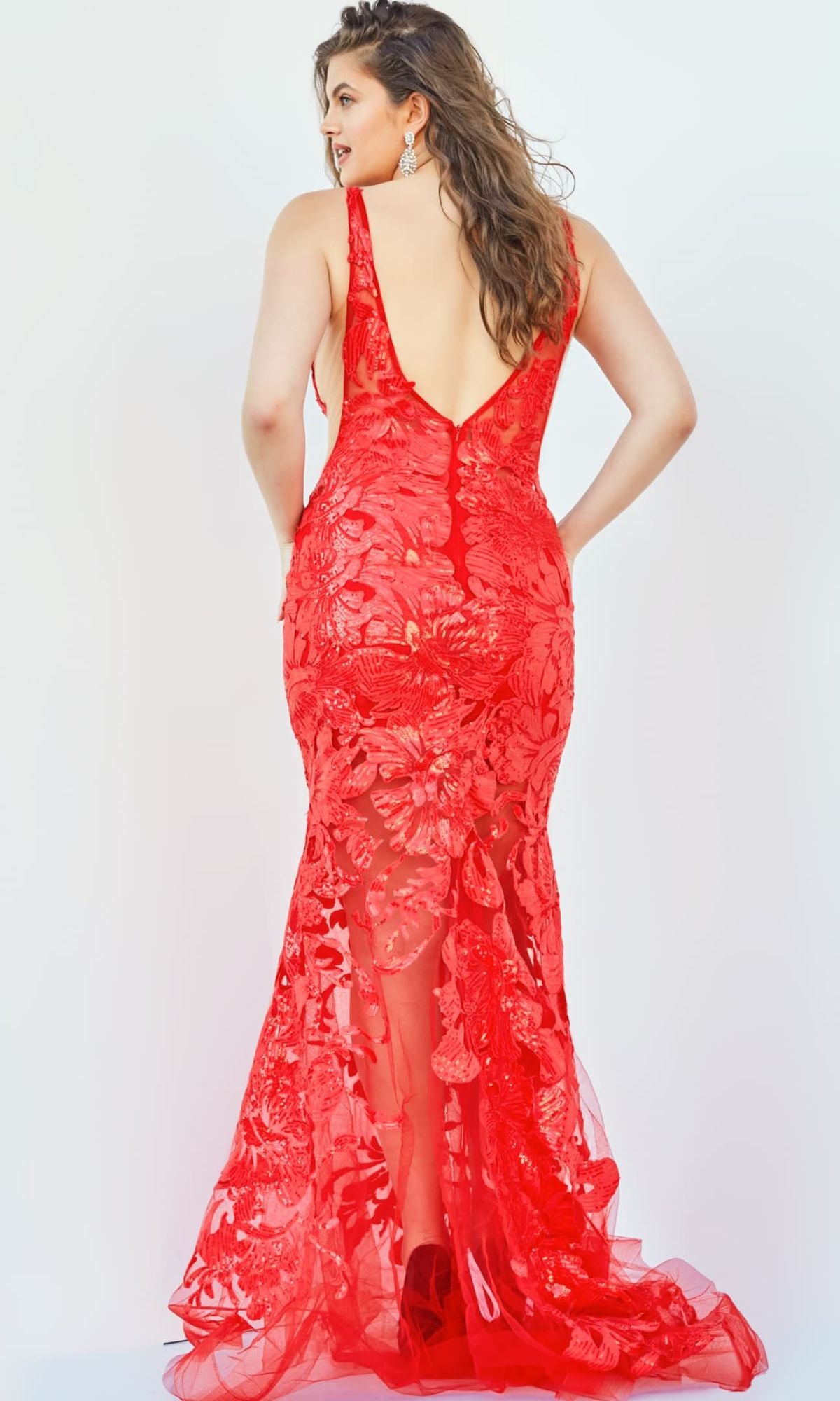 Woman wearing a fitted, sleeveless Jovani Plus-Size Sheer Prom Dress with sequins and a deep V back, standing and facing away from the camera against a plain light background.